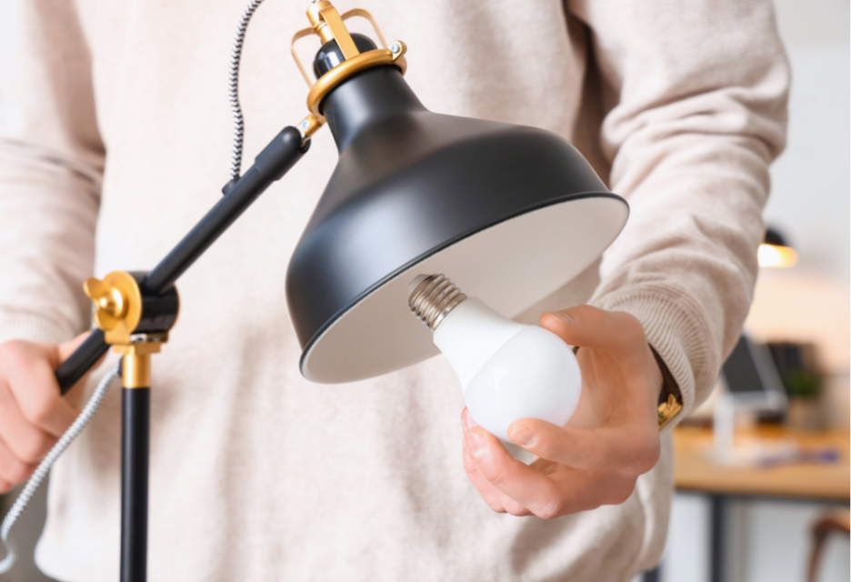 Close-up of a person replacing a light bulb in a black and gold desk lamp, illustrating lighting upgrades and energy-efficient improvements.